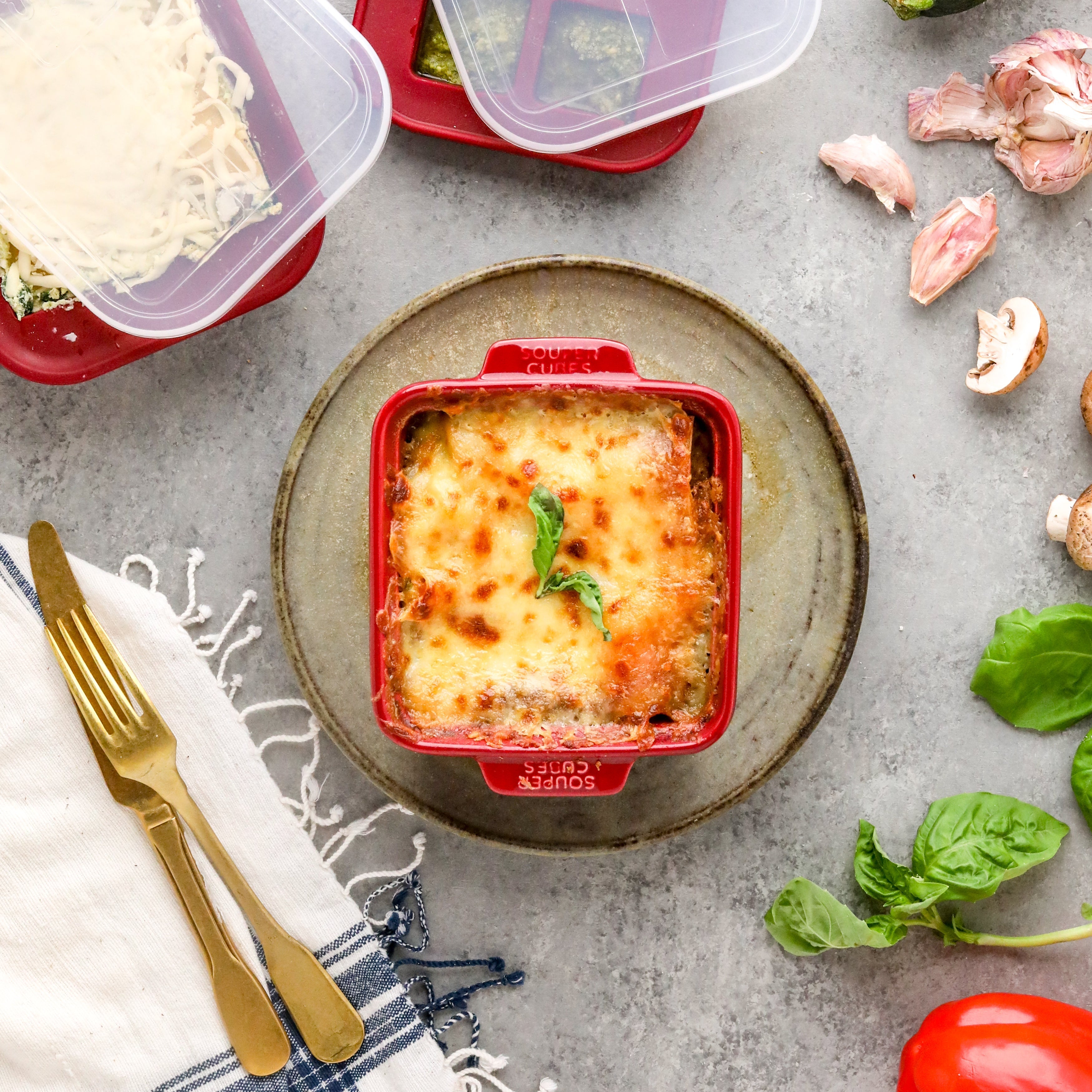 image of a lasagna baked in a red square baking dish on top of a plate next to two souper cubes trays