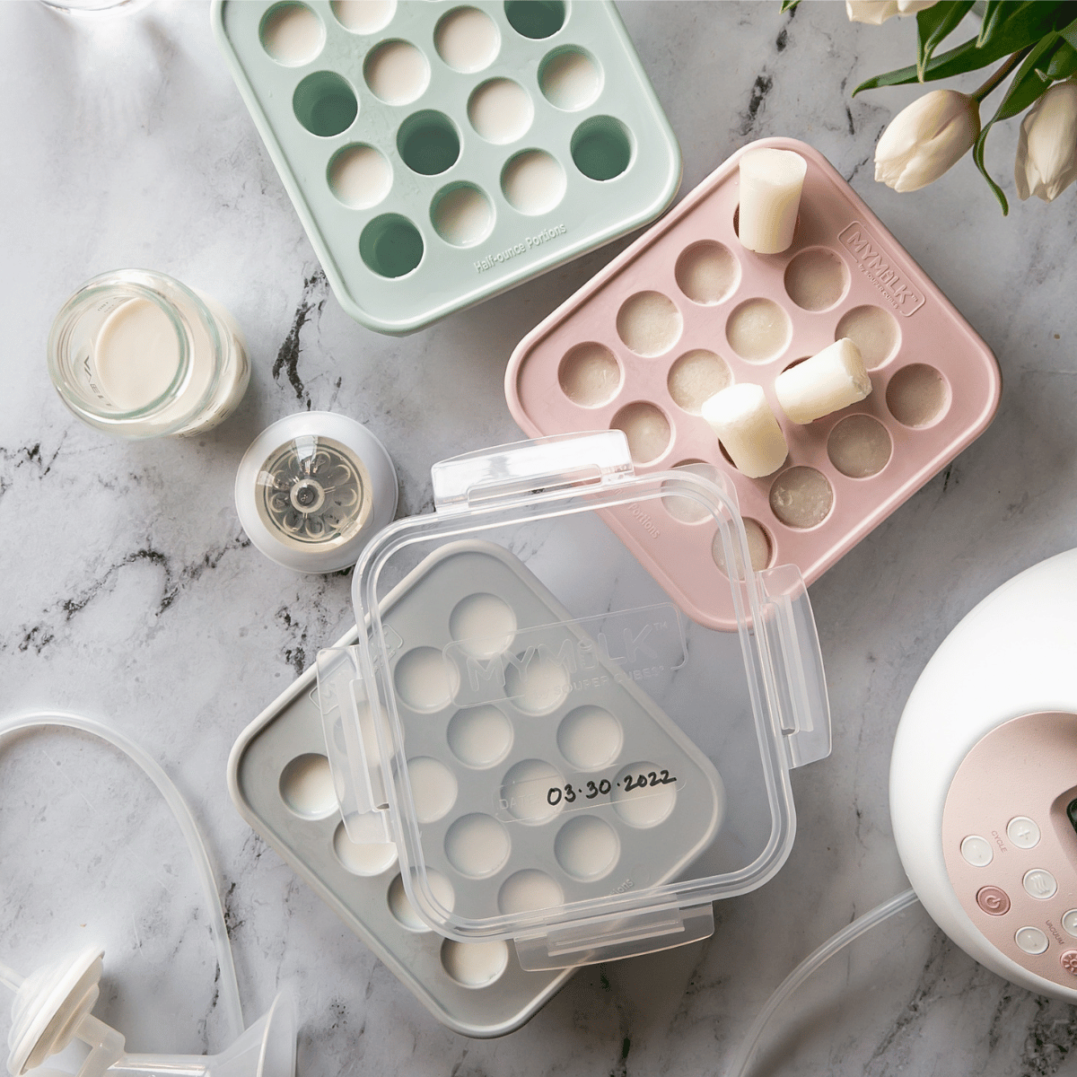 Set of silicone breast milk trays on a marble surface with flowers.