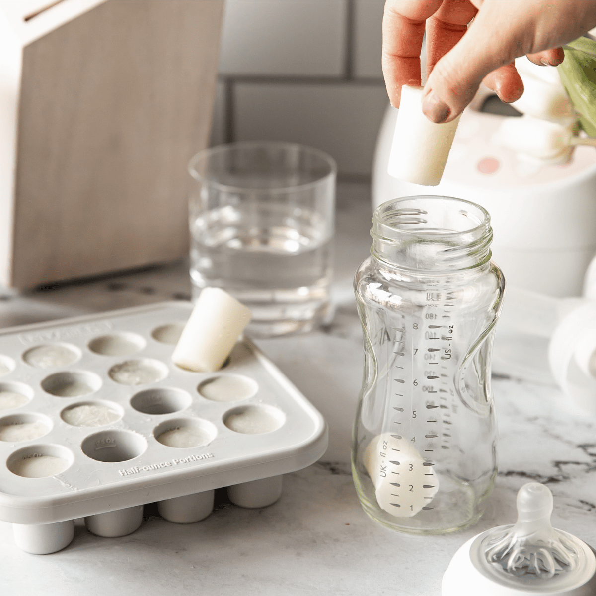 Person preparing baby bottles with MyMilk trays on a marble surface.