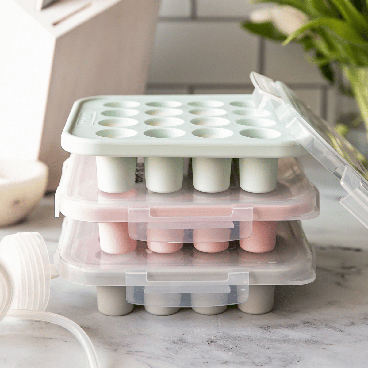Stackable breast milk trays with multiple compartments on a kitchen counter.