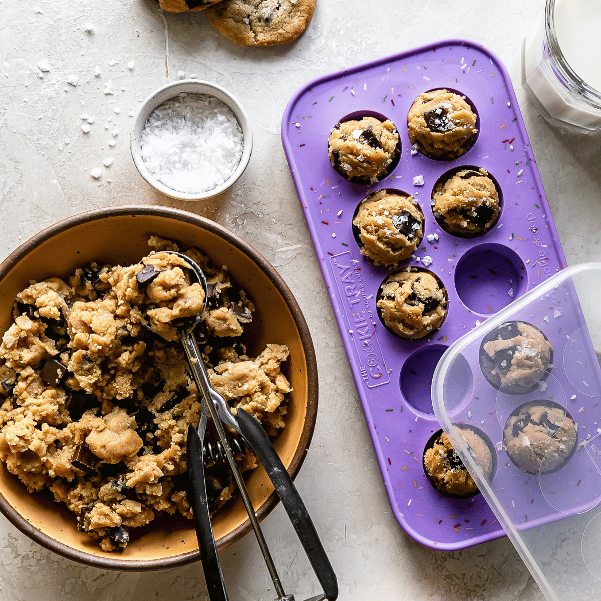 Cookie dough in a bowl with a purple silicone mold and baked cookies on a light surface.