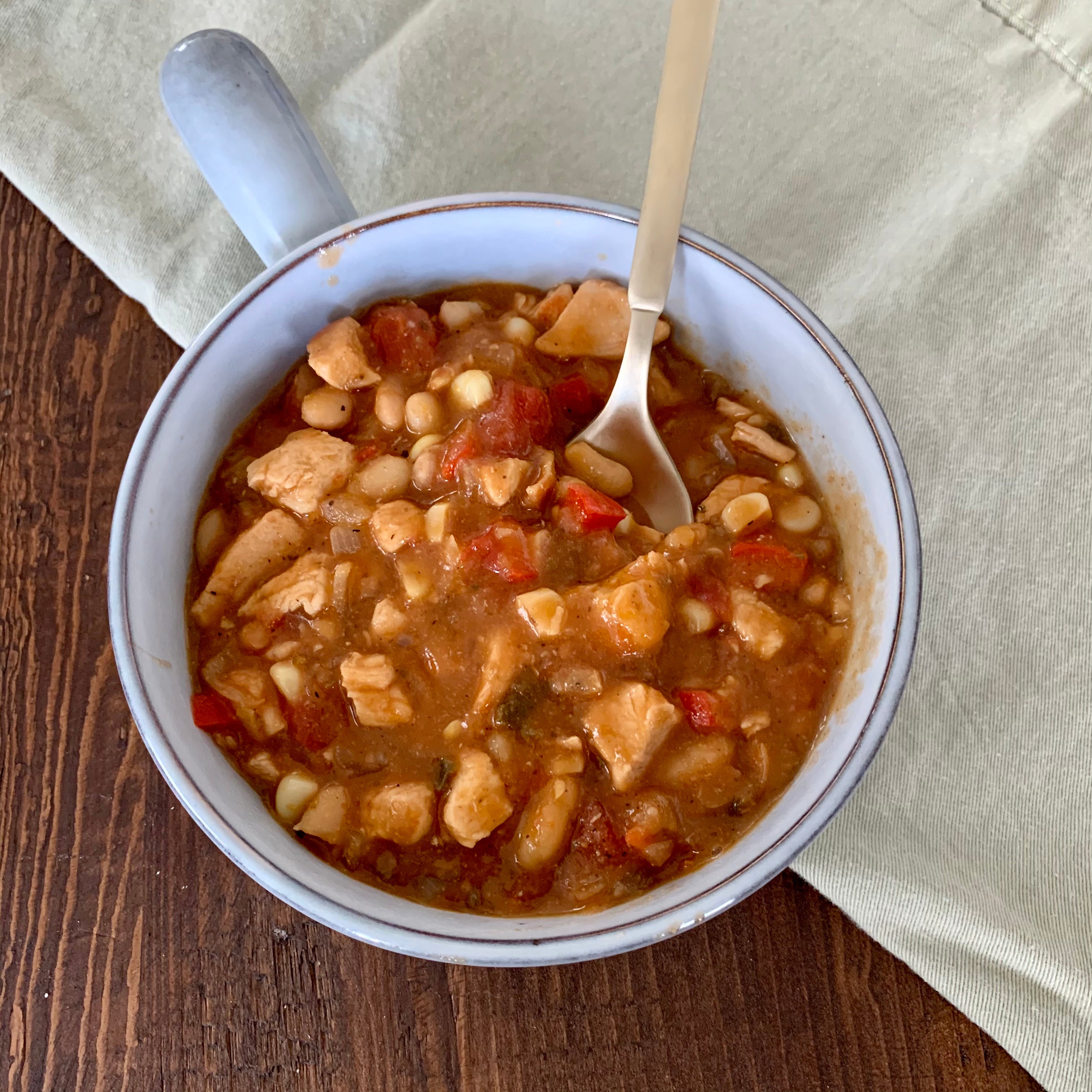 bowl of chicken chili on a wooden table next to a light green cloth napkin
