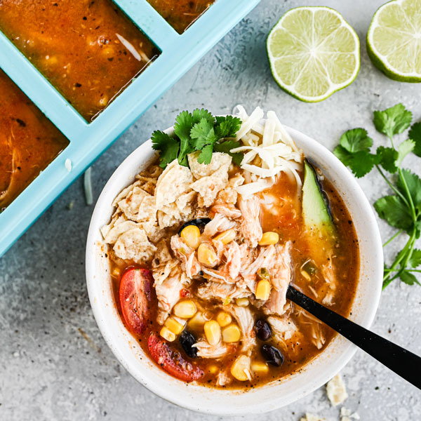 image of a bowl of chicken tortilla soup with garnishes near a souper cubes 1cup tray