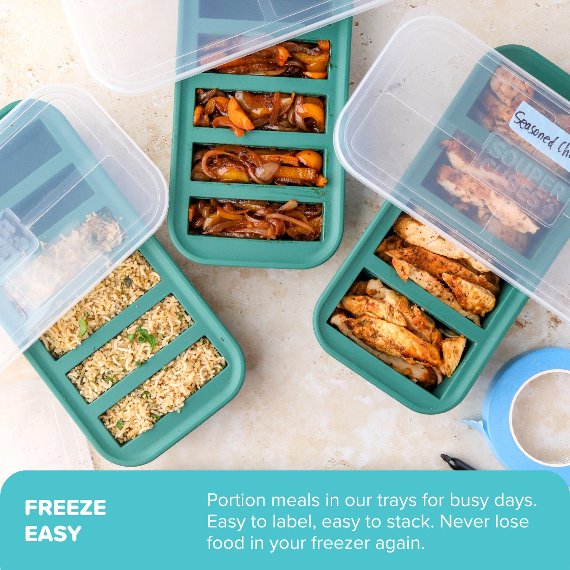 Three teal freeze-able meal prep trays with clear lids are arranged on a light stone surface, showing prepared foods like rice, pasta, grilled chicken, and sautéed vegetables. A teal text banner at the bottom reads 'FREEZE EASY' with descriptive copy, and a small blue tape dispenser is partially visible on the right.