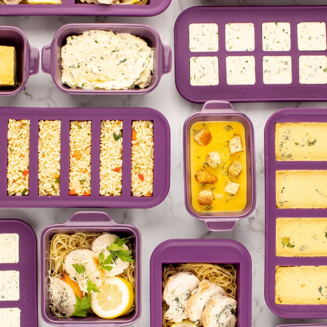 Purple silicone meal prep and baking trays arranged on a light marble surface, shown with various prepared foods 